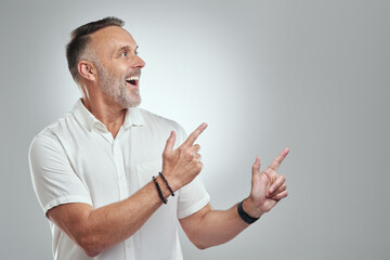 Fototapeta premium Mature, happy man and pointing with space in studio for advertising on a white background. Male person, model or showing with smile for option, choice or selection on mockup for marketing or tips
