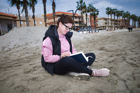 Woman sitting on the beach sand enjoying reading