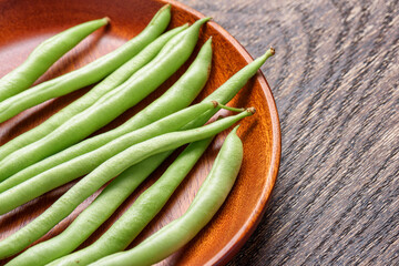 Closeup view of fresh green beans on wooden plate