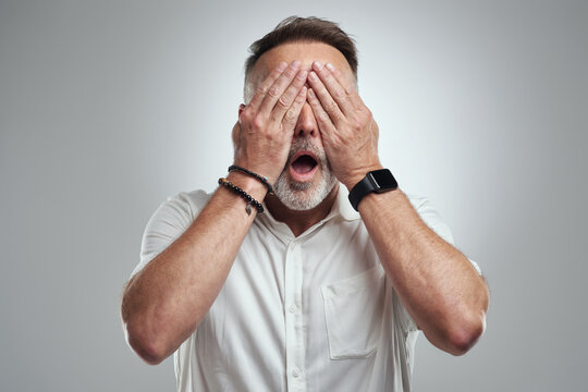 Mature, man and cover with eyes for fear, terror or shock on a white studio background. Male person, model or hidden with hands on face or embarrassment for mistake, disappointment or accident