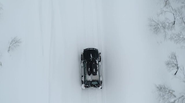 Vehicle driving across wide snowy plain in winter landscape top down view, aerial tracking follow