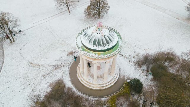 Calm drone panning over the Monopteros in English Garden Munich, capturing peaceful winter atmosphere with snow and soft sunlight.