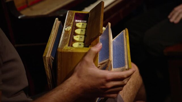 Musician playing a vintage wooden concertina, expanding the bellows while pressing button keys. Warm, dim lighting creates an intimate, rustic atmosphere. Close Up.