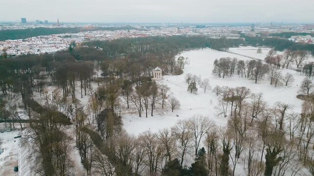 Drone footage advancing towards the Monopteros Munich in English Garden in Munich over a snowy winter landscape on a sunny christmas day.