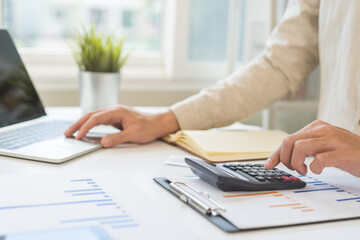Fototapeta premium Account finance, asian young business man hand using calculator, laptop computer for calculate budget, cost and income of company from paperwork, plan spend money expenses, working on desk at home.