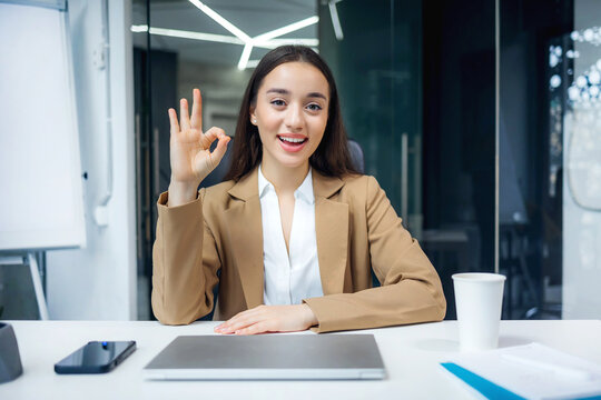 happy and successful female programmer inside office at workplace show ok sign, worker smiling and looking at camera satisfied with results of achievements at work