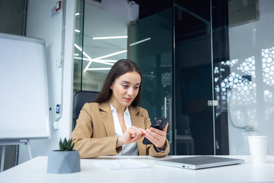 Cheerful woman sitting at table studying using phone take a break holding mobile phone surfing internet received message from friend chatting about weekend plans