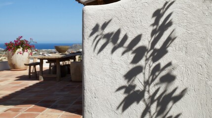A crisp, dark grey plant shadow cast against a sharp, bright white stucco wall in a sun-drenched Mediterranean patio with terracotta tiles, bougainvillea, and a blue ocean view.