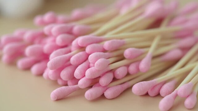 Wooden cotton swabs with pink tips lying on light surface in close up panning video clip.