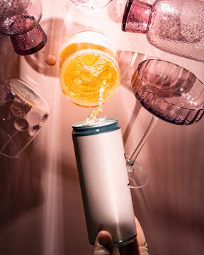 pink can of drink being poured into a glass surrounded by glasses