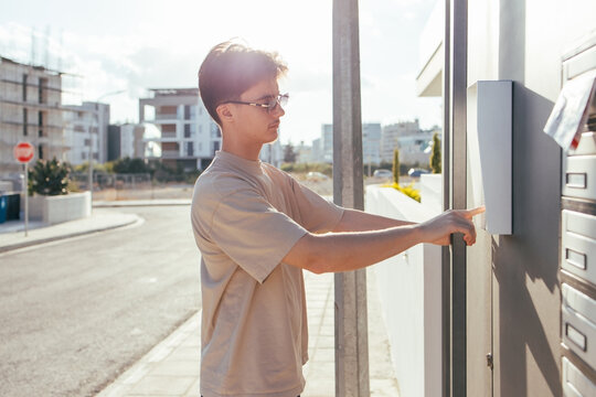 Young person pressing intercom button of residential complex