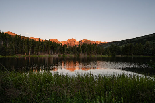 Sprague Lake reflecting sunlit mountains and pine trees at dawn