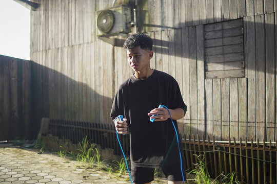 Young Asian athlete shadow boxing while holding skipping rope during outdoor HIIT workout