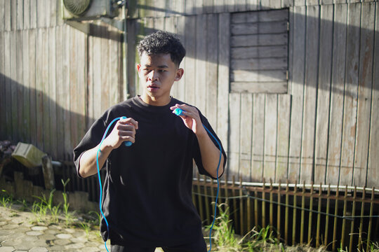 Young Asian athlete shadow boxing while holding skipping rope during outdoor HIIT workout