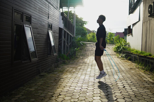Young Asian man skipping rope outdoors for fitness. Focused athletic male exercising cardio workout in home background, daylight