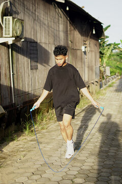 Young Asian man skipping rope outdoors for fitness. Focused athletic male exercising cardio workout in home background, daylight