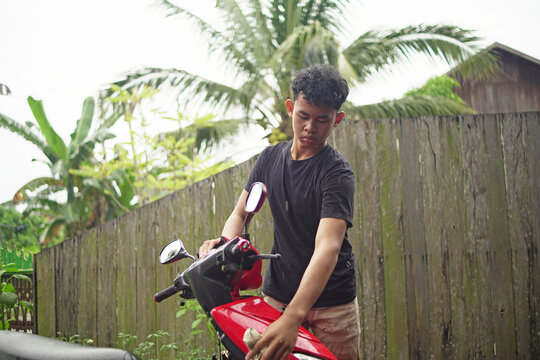 Young Asian man washing and wiping a red scooter at home backyard