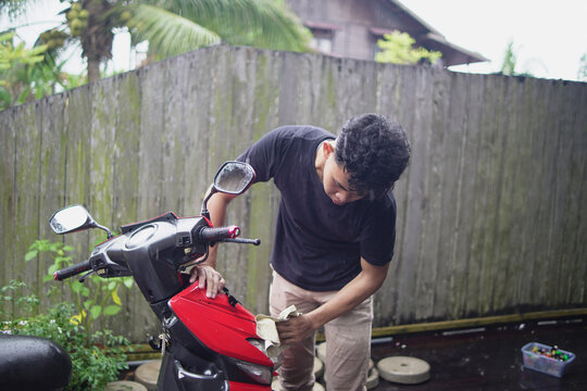 Young Asian man washing and wiping a red scooter at home backyard