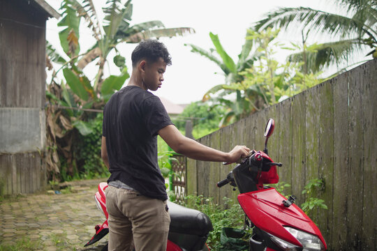 Young Asian man washing and wiping a red scooter at home backyard