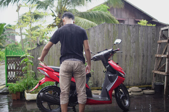 Young Asian man washing and wiping a red scooter at home backyard