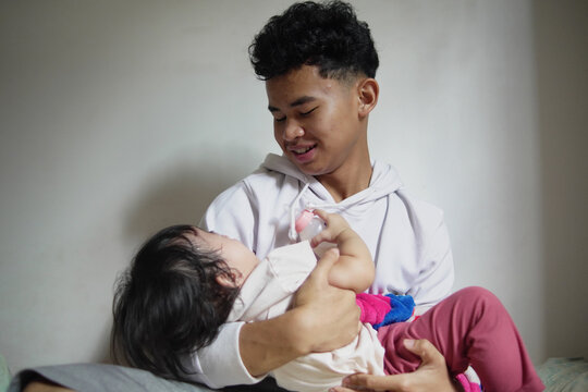Happy young man holding and playing with his baby sister in a warm candid moment at home