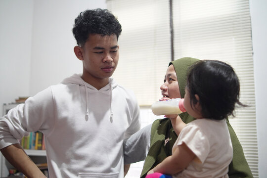 Happy young man talking to mother holding baby sister in candid family moment at home