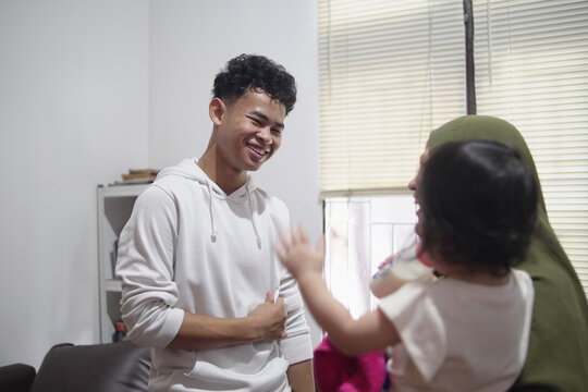 Happy young man talking to mother holding baby sister in candid family moment at home