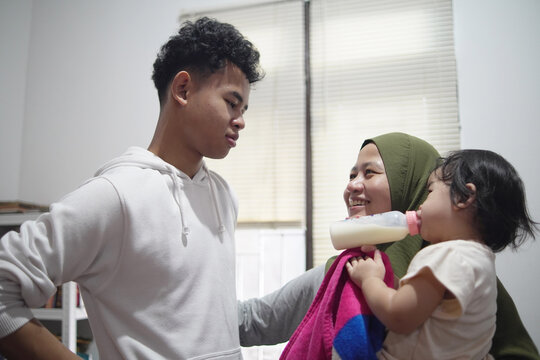 Happy young man talking to mother holding baby sister in candid family moment at home