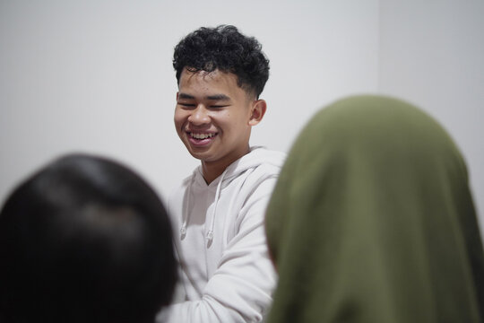 Happy young man talking to mother holding baby sister in candid family moment at home