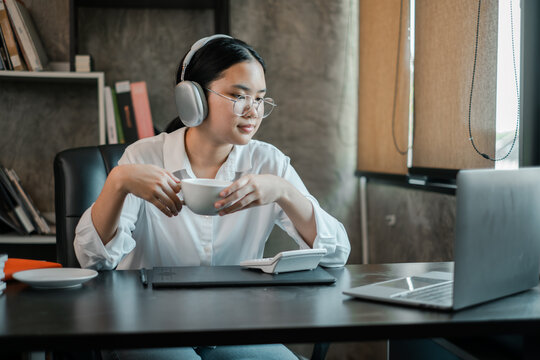 A focused young woman wearing headphones works on her laptop in a stylish home office environment.