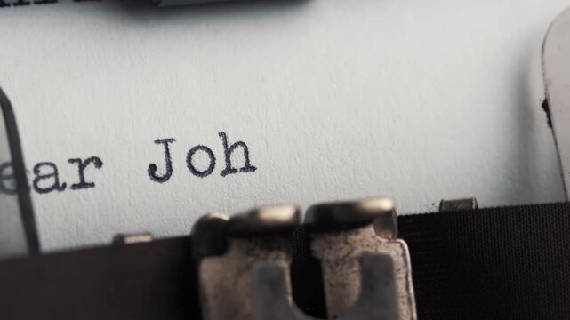 Letter is typed on typewriter paper with black ink addressed to John in a close-up view showing keys and paper with sign Dear John