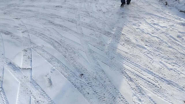 Footprints and tire tracks in fresh snow lead across a winter landscape, showcasing a progression of movement and interaction with the snowy ground