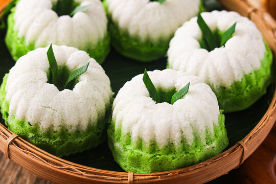 Closeup view of Kue Putu Ayu, the classic Indonesian steamed pandan cake. These soft, fluffy treats are topped with grated coconut. Captured with natural light on a wooden background.
