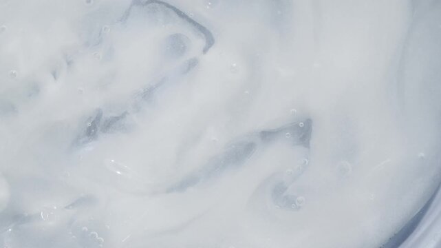 Macro of creamy white liquid with smooth swirls and soft bubbles, clean minimal texture for skincare or dairy concept, 4K