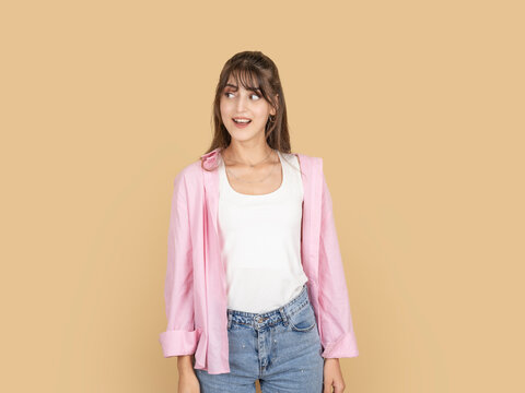 Surprised caucasian woman looking aside with excited expression, reacting to unexpected situation concept, wearing pink shirt and denim, isolated on beige studio background with copy space.