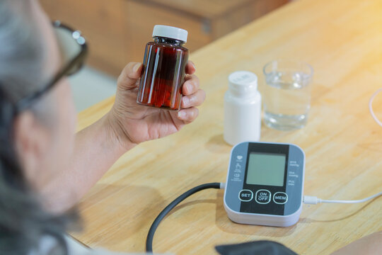 Rear view of senior woman holding a pill bottle while using medical device