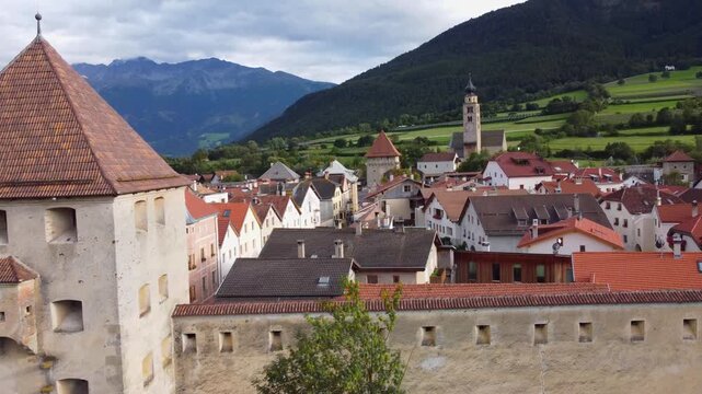 Aerial 4K drone view of Glorenza (Glurns) in South Tyrol, Italy. Beautiful medieval city walls, historic red-tiled roofs, and the Saint Pancras church tower set against the Alpine landscape