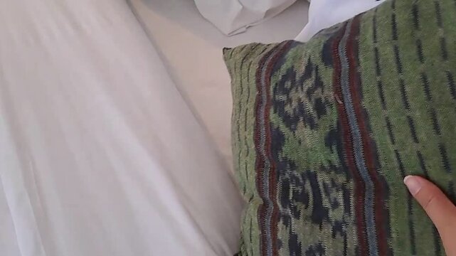 A close-up shot of a hand gently patting or smoothing a white bed sheet or cover.