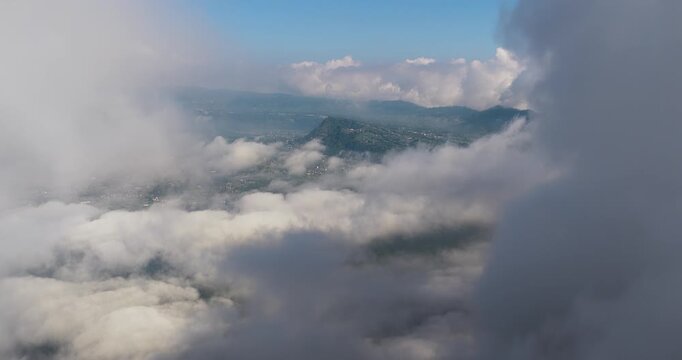 Aerial view of a landscape with green mountains partially covered by fluffy white clouds, creating a serene and dreamy vista, Kintamani, Bali, Indonesia.