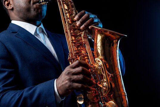Close up shot of African American man in elegant blue suit and white shirt playing tenor saxophone