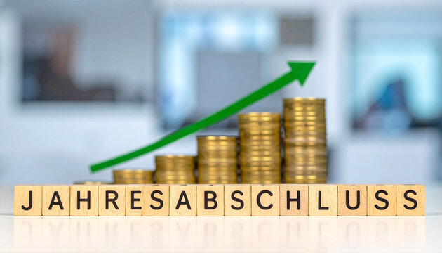 Holzklötze bilden das Wort "Jahresabschluss" auf Münzstapel , mit einen steigenden grünen Pfeil.