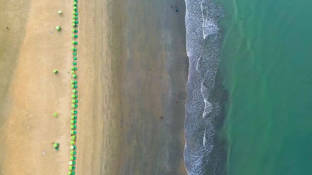 Aerial view of the beach showing the line of green umbrellas contrasting with the golden sand meeting the turquoise ocean, Cox's Bazar, Bangladesh.