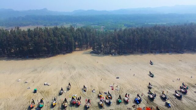 Aerial view of fishing boats lined along the sandy beach contrasting with lush green vegetation and the vast expanse of the ocean, Cox's Bazar, Bangladesh.