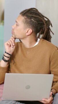Vertical video: Pausing, brown-sweater man lifting gaze, turning left on couch holding laptop
