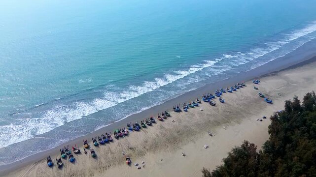 Aerial view of fishing boats lining the sandy beach with the contrast of the turquoise sea and the lush green trees, Cox's Bazar, Bangladesh.