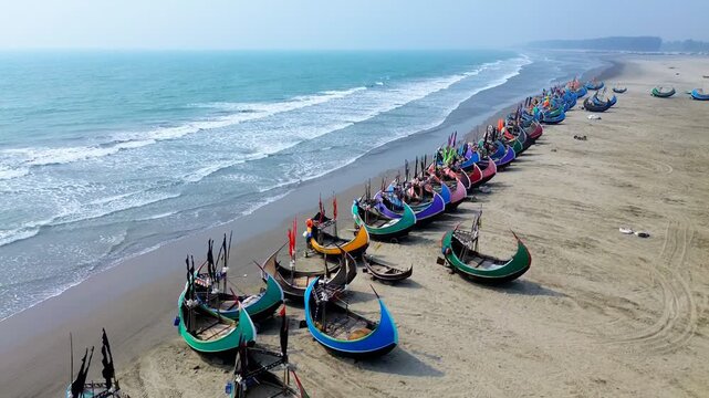Aerial view of fishing boats rest on sandy shore, colorful against the turquoise sea, creating a vibrant contrast, Cox's Bazar, Chittagong Division, Bangladesh.