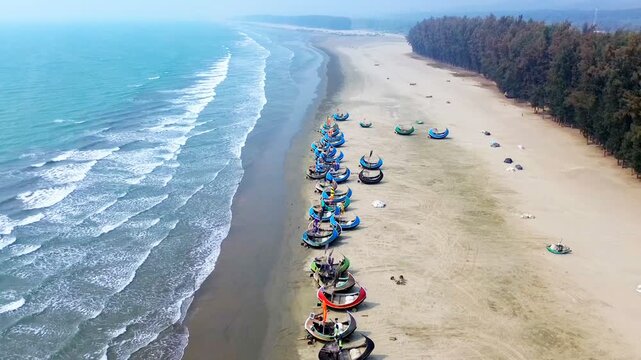 Aerial view of fishing boats resting on the sandy beach contrasting with the turquoise sea and the lush green trees, Cox's Bazar, Chittagong Division, Bangladesh.