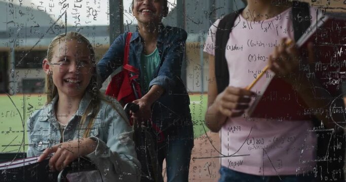 Three female schoolchildren walking in covered corridor, pushing wheelchair, holding red notebook