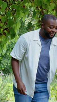 Vertical video: Spotting berries, father in white shirt pointing under garden tree, showing son