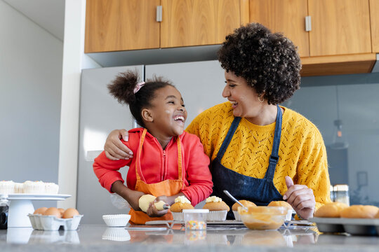 African American mother and daughter frosting cupcakes on counter in kitchen, with sprinkles